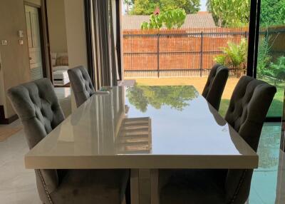 Modern dining room with glass table and upholstered chairs next to large sliding glass doors overlooking a backyard