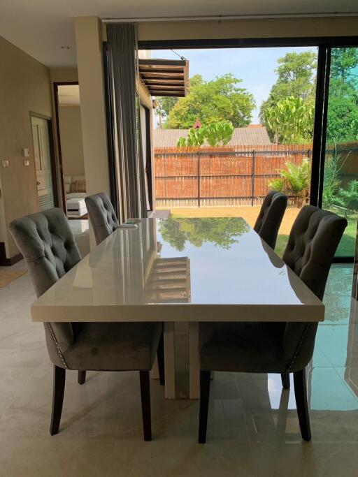 Modern dining room with glass table and upholstered chairs next to large sliding glass doors overlooking a backyard