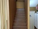 Staircase with wooden steps leading to the upper floor, adjacent to a white door and curtain