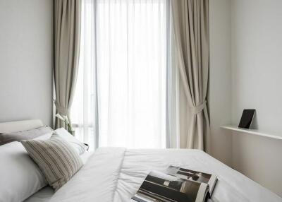 A minimalistic styled bedroom with natural light, white linens, and floor-length curtains