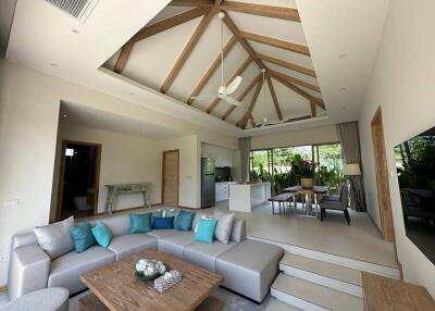 Spacious living room with high ceiling and wooden beams, featuring a modern kitchen and dining area.