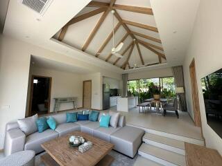 Spacious living room with high ceiling and wooden beams, featuring a modern kitchen and dining area.