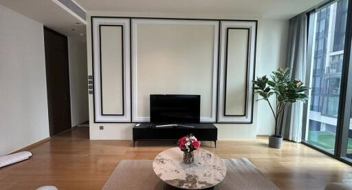 Modern living room with TV, coffee table, indoor plant, and large windows