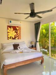 Well-lit bedroom with a large window, bed, wall art, and ceiling fan