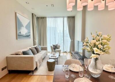 Modern living room with a dining area, featuring a sofa, coffee table, TV setup, and a vase with flowers on the dining table.