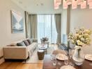 Modern living room with a dining area, featuring a sofa, coffee table, TV setup, and a vase with flowers on the dining table.