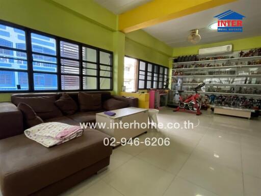 Cozy living room with large windows, a brown sectional sofa, and a display shelf with collectibles