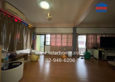 Main living space with brown floor, beige curtains, ceiling fan, TV, and window air conditioner.