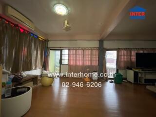 Main living space with brown floor, beige curtains, ceiling fan, TV, and window air conditioner.