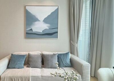 Modern living room with white sofa, cushions, artwork, and large windows with curtains