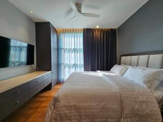 Modern bedroom with large bed, wall-mounted TV, and ample natural light