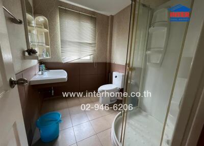 A well-maintained bathroom with a glass shower enclosure, sink, toilet, and window with blinds.