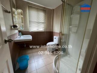 A well-maintained bathroom with a glass shower enclosure, sink, toilet, and window with blinds.