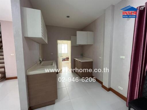 Neutral tone kitchen with base and wall cabinets, sink, and adjoining rooms