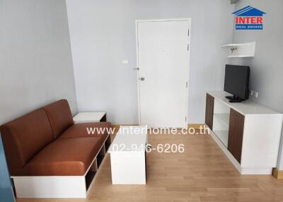 Living room with a brown sofa, white coffee table, TV on a stand, and a door