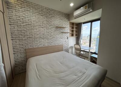 Modern bedroom with a large bed, brick accent wall, window view, air conditioner, and study area