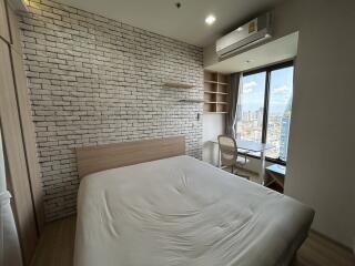 Modern bedroom with a large bed, brick accent wall, window view, air conditioner, and study area