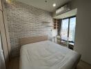 Modern bedroom with a large bed, brick accent wall, window view, air conditioner, and study area