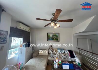 A cozy living room with a couch, fan, and wall-mounted air conditioning unit.