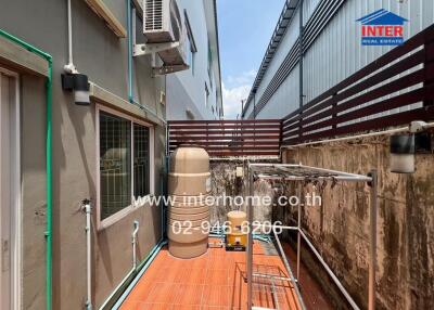 A view of a narrow outdoor space with air conditioning unit and a large water tank