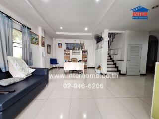 Spacious, well-lit living room with tile flooring, a black sofa, and a desk area