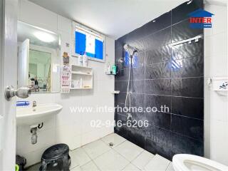 A clean bathroom with a shower area, sink, mirror, and small shelf.