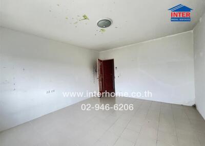 Empty room in a property with white walls, tiled floor, a red door, ceiling light fixture, and contact information on a website address