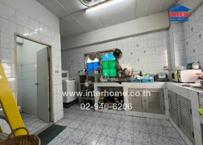 A well-equipped kitchen with tiled walls and floors, featuring countertops, sinks, cabinets, and appliances