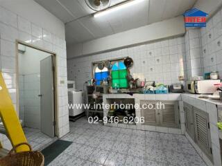 A well-equipped kitchen with tiled walls and floors, featuring countertops, sinks, cabinets, and appliances