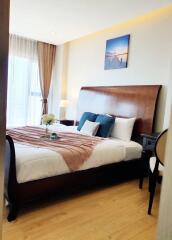 Cozy bedroom with wooden bed frame, decorative pillows, wall art, and natural lighting from large window