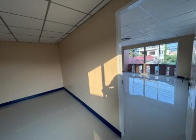 Empty room with tiled floor and open door leading to another room with large windows