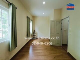 Bright bedroom with wooden flooring, green curtains, and a window allowing natural light.