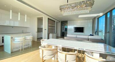 Spacious modern living and dining area with large windows, kitchen island, white furniture, and chandelier