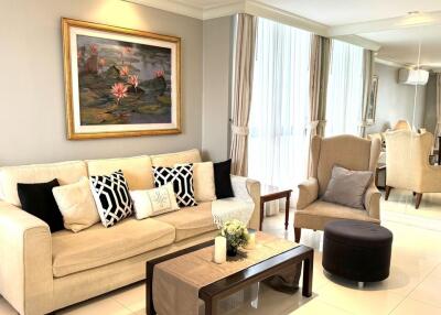 Elegant living room with a beige couch, wall art, coffee table, armchair, and large windows with curtains.