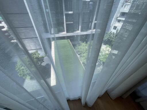 View from window with sheer curtains, overlooking courtyard with green space