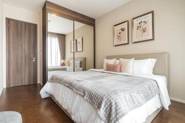 Well-lit bedroom with wooden flooring, large mirror, and cozy bedding