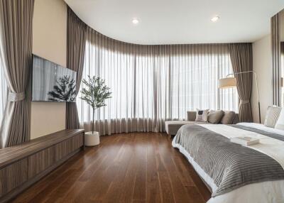 Modern bedroom with wooden flooring, large windows, and drapes