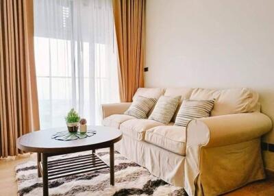 Cozy living room with a beige sofa, coffee table, and large window with curtains