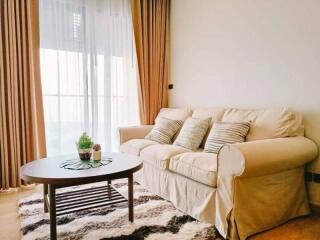 Cozy living room with a beige sofa, coffee table, and large window with curtains