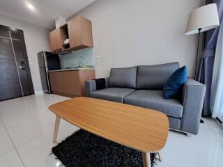 Modern living room with a grey sofa, wooden coffee table, and small kitchenette