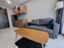 Modern living room with a grey sofa, wooden coffee table, and small kitchenette