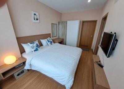 A modern bedroom with a bed, side table, wardrobe, wall-mounted TV, and wooden flooring.