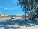 Street view with a white car and a truck parked under a tree