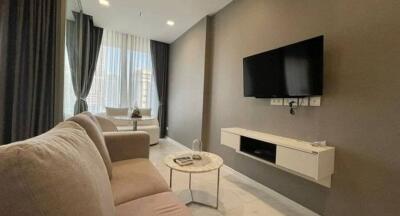 Modern living room with a wall-mounted TV, a cozy sofa, and large windows.