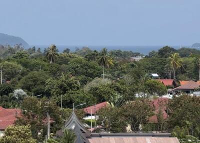 Scenic view of a neighborhood with trees, red rooftops, and ocean in the background