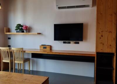 Cozy bedroom with wooden elements, air conditioner, wall-mounted TV, and a study area with chairs