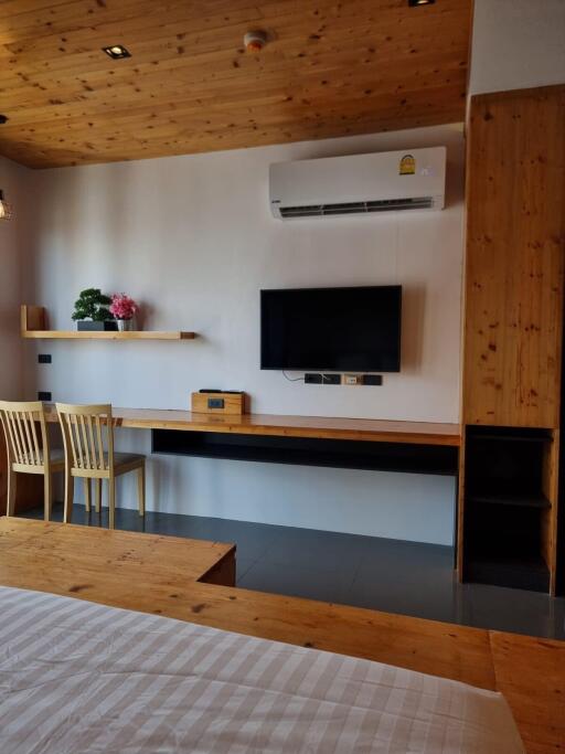Cozy bedroom with wooden elements, air conditioner, wall-mounted TV, and a study area with chairs