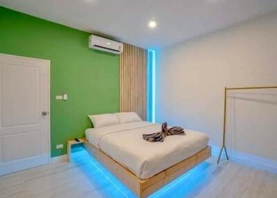 Modern bedroom with a green accent wall, air conditioning, and lit under-bed lighting