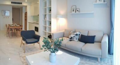 Modern living room with a grey couch, armchair, wall shelves, and a kitchen in the background