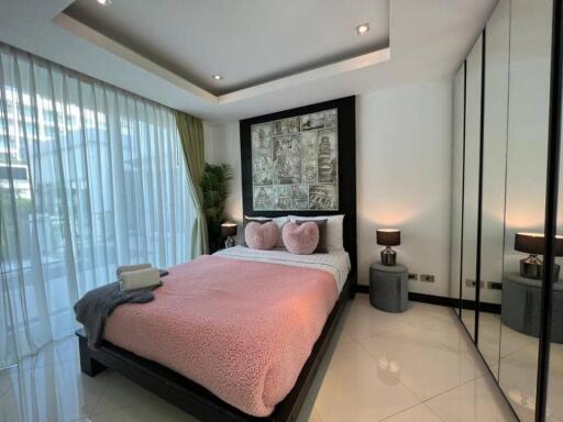 Modern bedroom with large windows, pink bedding, and mirrored wardrobe